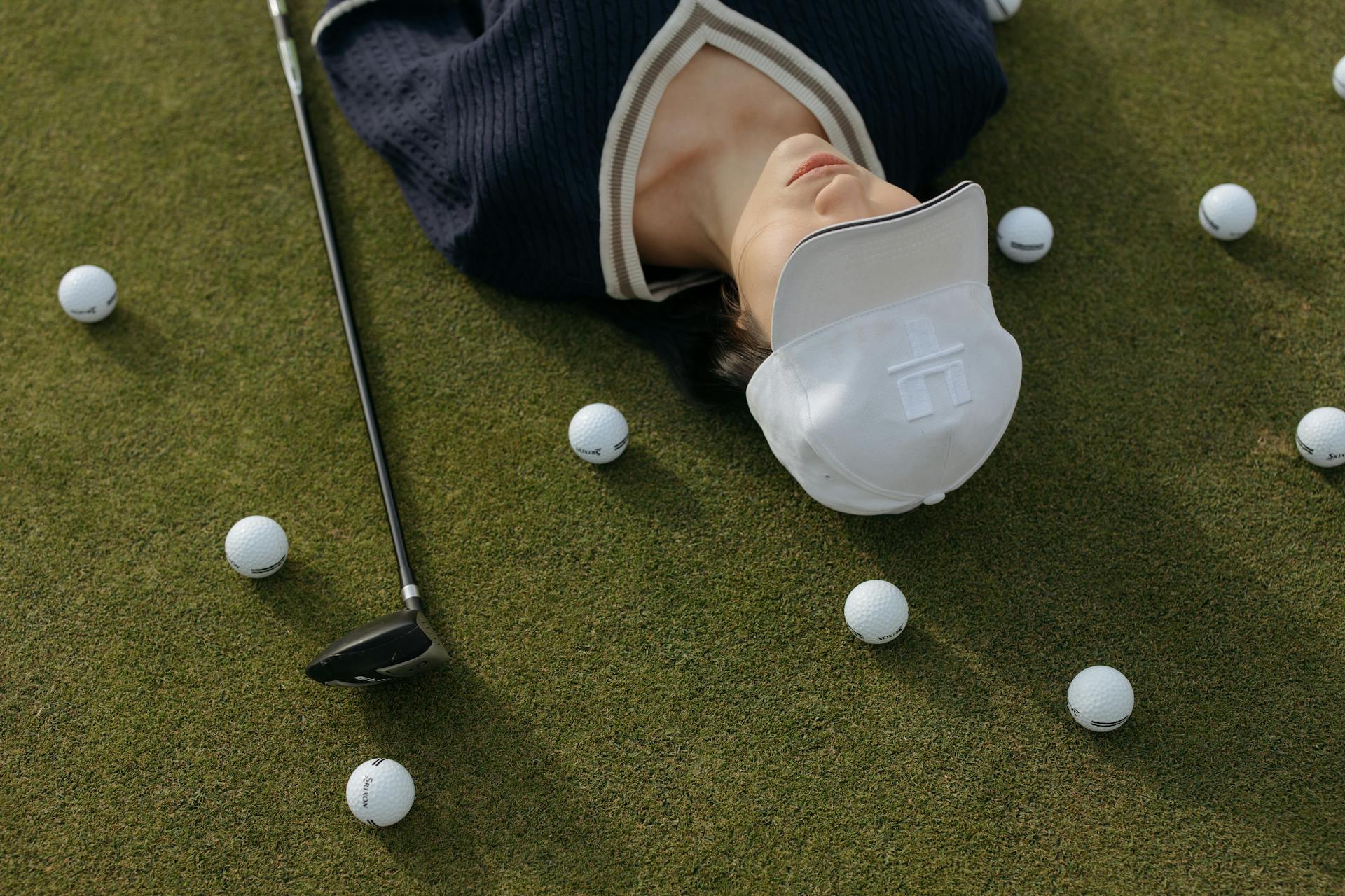 woman in cap lies on grass with golf balls around her